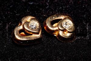 Gold heart-shaped earrings with diamonds on a black background. photo