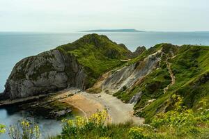 Scenic view of a coastal landscape with cliffs, a beach, and a winding path leading to the sea. photo