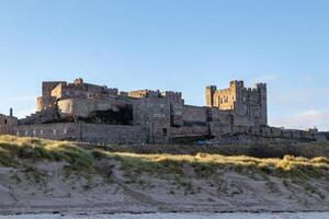 Majestic medieval castle on a sandy beach under a clear blue sky at dusk. photo