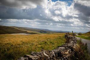 Rustic stone wall along a country road with rolling hills and dramatic cloudscape in the background. photo