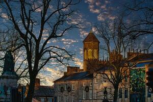 Historic stone building with a clock tower at dusk, silhouetted trees, and a vibrant sky in Lancaster. photo