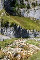 Scenic view of a rocky mountain slope with a green grassy area and a small stream in the foreground. photo
