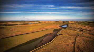 Scenic aerial view of a winding river through a vast, colorful landscape under a blue sky with clouds at Sycamore Gap, Northumberland, UK. photo