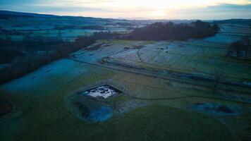 Aerial view of a tranquil countryside landscape at dusk with fields, a pond, and the horizon under a gradient sky. photo