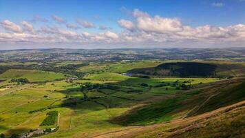 Panoramic view of a lush green valley with rolling hills under a blue sky with scattered clouds in Pendle Hill, England. photo