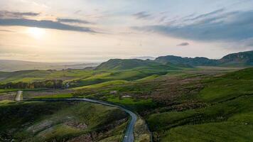 Scenic view of a winding road through lush green hills with a sunset backdrop. photo