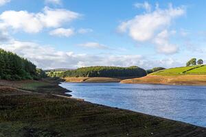 Serene landscape with a calm lake, surrounded by green hills and a clear blue sky with scattered clouds. photo