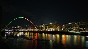 noche paisaje urbano con iluminado arco iris puente reflejando en agua en Newcastle sobre Tyne foto