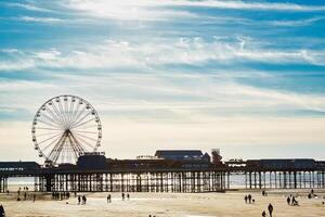 puesta de sol a un playa con un ferris rueda en un muelle y personas caminando en el arena en piscina negra, Inglaterra. foto