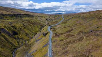 Aerial view of a vast, undulating landscape with green hills, a winding road, and overcast skies. photo