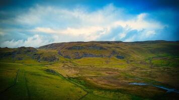 Scenic view of lush green fields leading up to a rugged mountain under a blue sky with clouds. photo