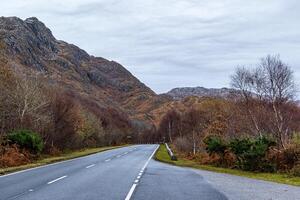 Empty road leading through a scenic autumn landscape with colorful foliage and mountain backdrop. photo