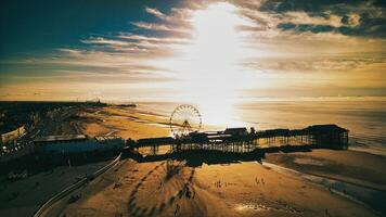 Aerial view of a beachfront with a pier and ferris wheel at sunset, casting long shadows in Backpool, England. photo