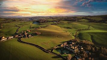 Aerial view of a picturesque rural landscape at sunset with rolling hills, a winding road, and a small village. photo