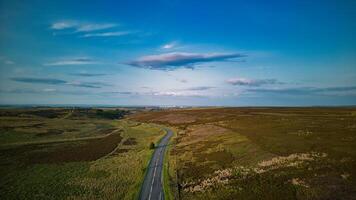 Aerial view of a winding road through a vast, open landscape with blue skies and scattered clouds in Yorkshire. photo