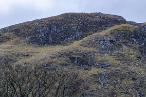 Rugged mountain terrain with sparse vegetation under an overcast sky in Scotland. photo