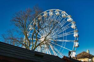 Ferris wheel against a clear blue sky, partially obscured by a rooftop, with bare trees in the background in Lancaster. photo