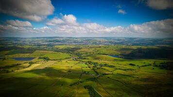Aerial view of lush green countryside with fields, trees, and a lake under a partly cloudy sky in Pendle Hill, England. photo