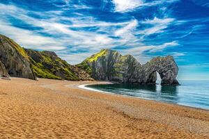 Scenic view of a beach with a large rock formation, clear blue sky, and calm sea at Durdle Door photo