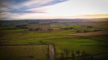 Aerial view of a countryside road at sunset with lush green fields and a soft, colorful sky at Sycamore Gap, Northumberland, UK. photo