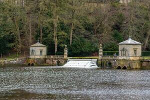 Historic stone buildings by a river with a small waterfall and lush greenery in the background. photo