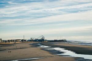 Serene beachscape with a distant pier, reflective tidal pools, and a few people enjoying the vast sandy shore under a cloudy sky in Blackpool, England. photo