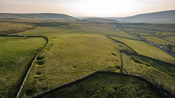 Aerial view of rolling green hills with patchwork fields and country roads at sunset in Peak District, England. photo