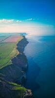 aéreo ver de un costero paisaje con acantilados, campos, y el Oceano reunión debajo un claro azul cielo en archivo, Inglaterra. foto