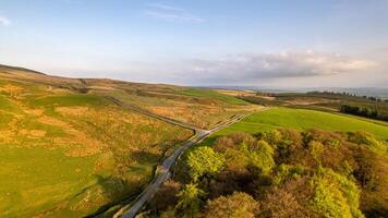 Aerial view of a winding road through lush green countryside with hills under a clear sky. photo