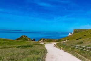 Scenic coastal pathway with lush green grass, blue sky, and calm sea, ideal for travel and nature themes at Durdle Door, England. photo