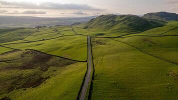 Aerial view of a winding road through lush green rolling hills under a soft light at dawn or dusk. photo