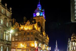 Illuminated historic building at night with clock tower, city lights, and clear sky. photo