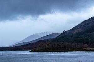 Misty mountain landscape with lake in the foreground under overcast sky in Scotland. photo