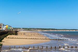 Sunny beachscape with wooden pier, colorful buildings, and people enjoying the shore, clear blue sky above in Bridlington, England. photo