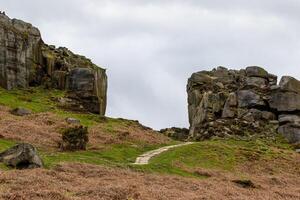 devanado camino mediante escabroso terreno con rocoso afloramientos y verdor debajo un nublado cielo en ilkley, Yorkshire foto