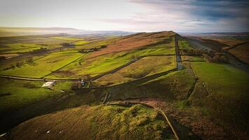 Aerial view of a scenic countryside road winding through green hills with dramatic lighting and expansive views at Sycamore Gap, Northumberland, UK. photo