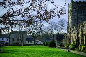 Quaint village with historic stone church, green lawn, and early spring foliage under a clear sky. photo