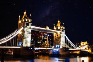 Night view of Tower Bridge in London with illuminated lights and starry sky. photo