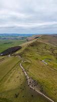 aéreo ver de un devanado sendero con caminantes en un lozano verde paisaje con laminación colinas debajo un nublado cielo en pico distrito, Inglaterra. foto