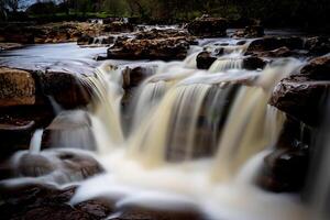 sereno cascada cascada terminado rocas con lozano verdor en el fondo, exhibiendo de la naturaleza tranquilidad en Yorkshire valles. foto