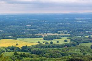 Scenic view of a lush countryside with rolling hills, fields, and forests under a cloudy sky. photo