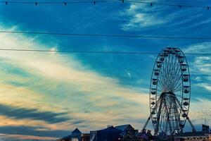 Ferris wheel silhouette against a vibrant sunset sky with clouds, urban skyline in the foreground in Blackpool, England. photo