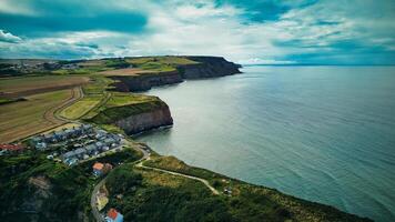 Aerial view of a coastal village with cliffs and farmland under a cloudy sky in Staithes, England. photo