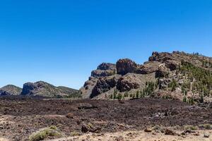 Volcanic landscape with rugged mountains and lava fields under a clear blue sky in the Teide, National Park, Tenerife photo