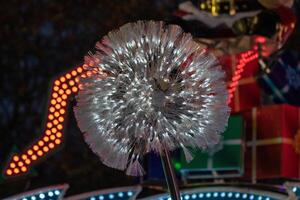 Illuminated dandelion-like light installation at night with blurred amusement park rides in the background. photo
