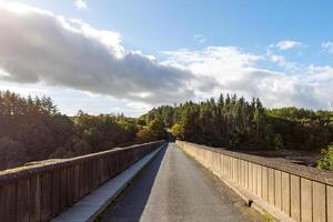 soleado día ver de un vacío la carretera con un de madera cerca líder mediante un lozano verde paisaje debajo un parcialmente nublado cielo. foto