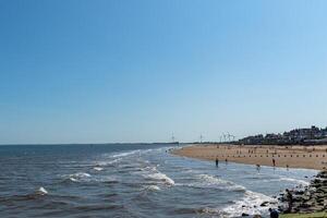 Sunny beachscape with waves, sandy shore, and distant wind turbines in Bridlington, England. photo