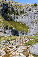 Scenic view of a rocky mountain with a green slope and a small stream in the foreground under a clear blue sky. photo
