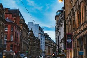 Dusk view of a bustling city street with historic architecture and glowing street lights under a blue sky in Manchester, England. photo