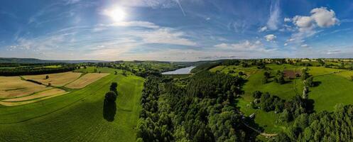 Panoramic view of a lush green valley with a river, under a vast blue sky with scattered clouds. photo